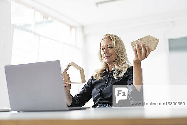Weibliche Unternehmerin hält ein Modell zu Hause  während sie den Laptop auf dem Schreibtisch im Heimbüro betrachtet