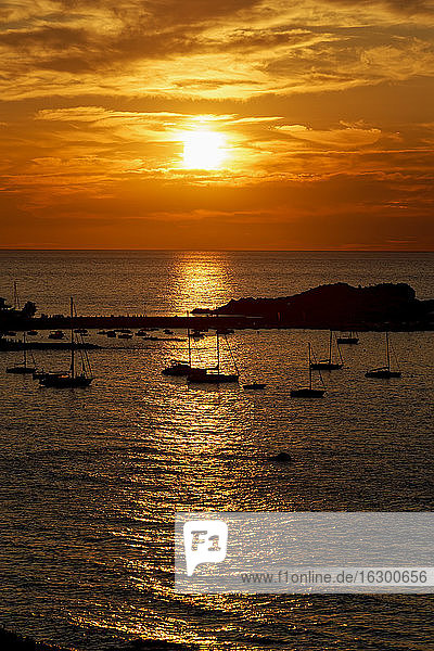 France  Haute-Corse  LIle-Rousse  Silhouettes of sailboats in front of small Mediterranean island at moody sunset