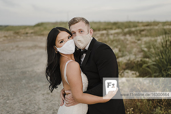 Braut mit Bräutigam mit Gesichtsschutzmaske im Feld während COVID-19