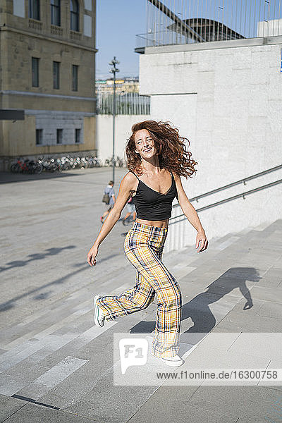 Fröhliche rothaarige Frau  die sich auf einer Treppe in der Stadt an einem sonnigen Tag bewegt