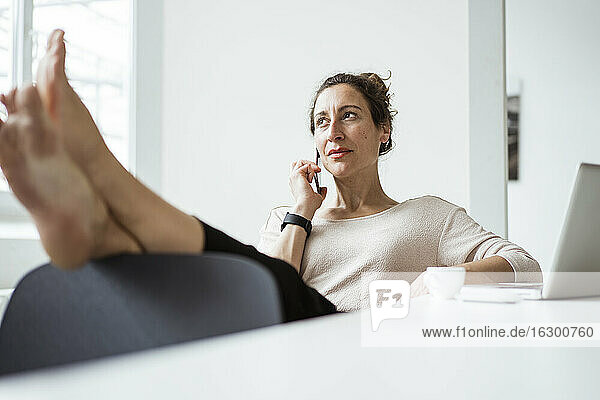 Geschäftsfrau mit Füßen auf dem Tisch  die beim Entspannen über ein Smartphone spricht