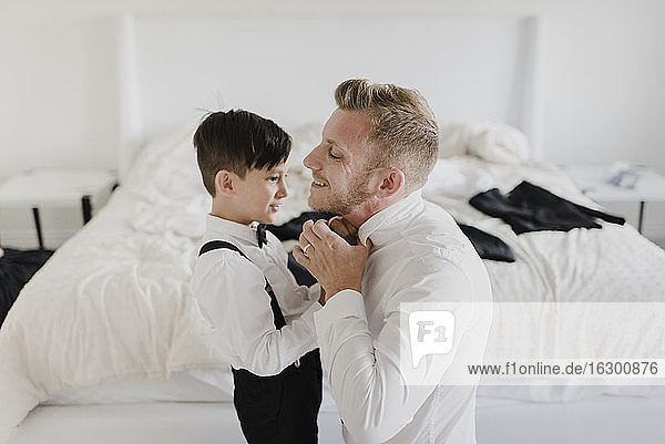 Lächelnder Vater und Sohn,  die sich im Schlafzimmer für die Hochzeit anziehen