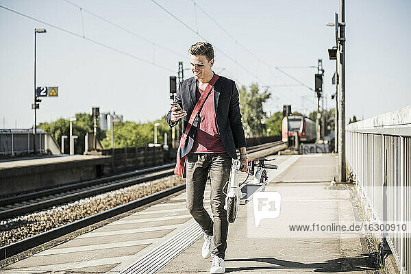 Mann mit Tretroller benutzt Handy beim Gehen auf dem Bahnsteig