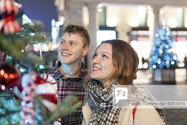 Happy young couple looking at Christmas tree and lights while standing in city