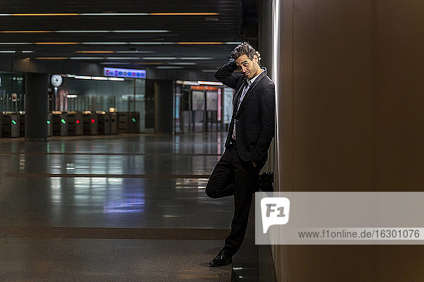 Thoughtful male professional wearing suit standing by wall at station