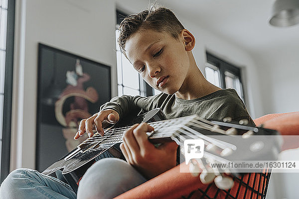 Nahaufnahme eines Jungen  der Gitarre spielt  während er zu Hause auf einem Stuhl sitzt