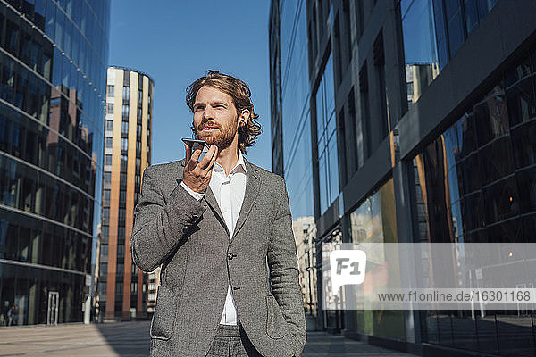 Selbstbewusster  gutaussehender Mann  der mit seinem Smartphone über einen Lautsprecher im Finanzviertel spricht