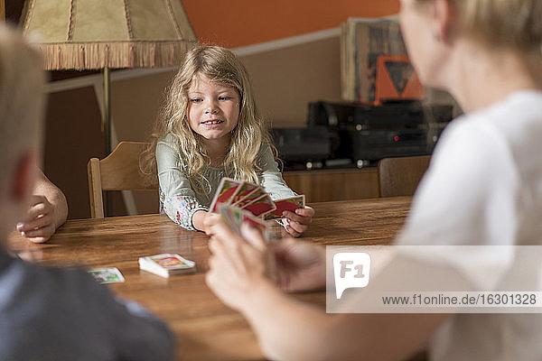 Nettes blondes Mädchen spielt Karten mit Familie am Esstisch