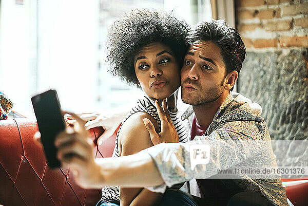 Couple puckering lips while taking selfie with smart phone while sitting in cafe