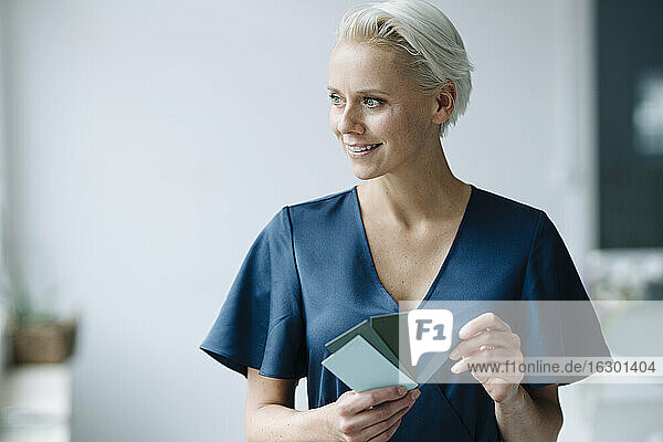 Close-up of smiling businesswoman holding color swatch looking away in office