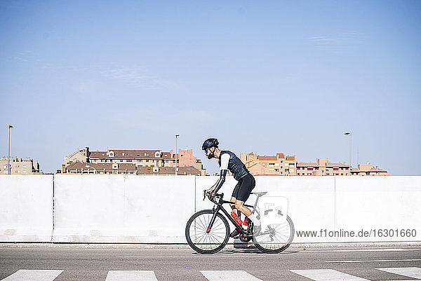 Männlicher amputierter Radfahrer  der mit dem Fahrrad auf der Straße gegen einen klaren blauen Himmel an einem sonnigen Tag fährt