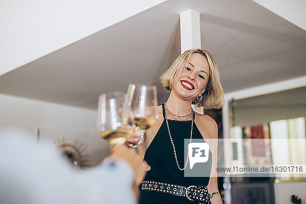 Lächelnde junge Frau stößt mit Weingläsern während einer Party zu Hause an