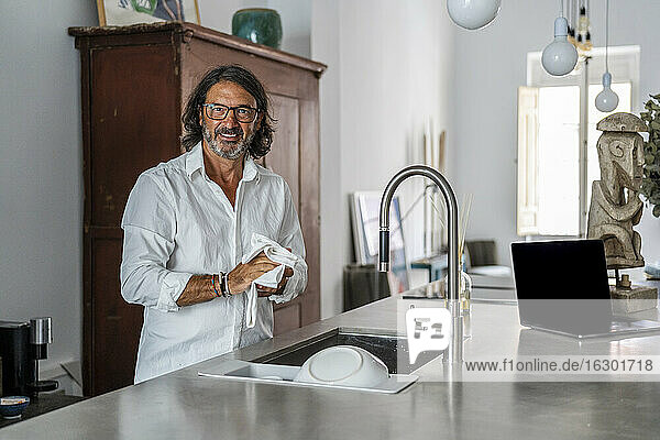 Lächelnder Mann beim Reinigen von Geschirr am Spülbecken in der Küche