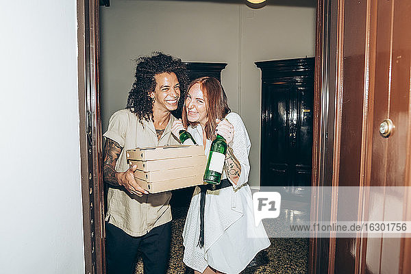 Cheerful friends with beer bottle and pizza boxes at entrance of home during party