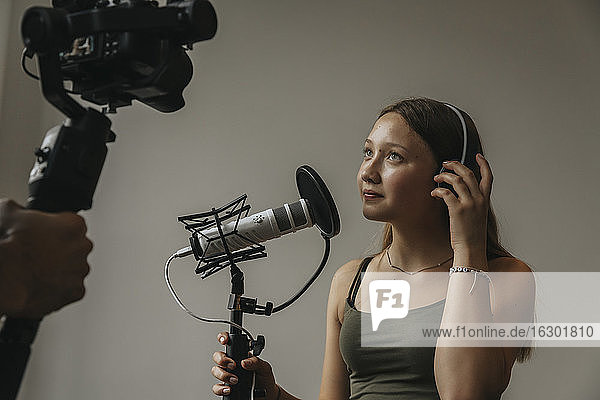 Teenager-Mädchen schaut in die Kamera und singt über Mikrofon an der Wand im Studio