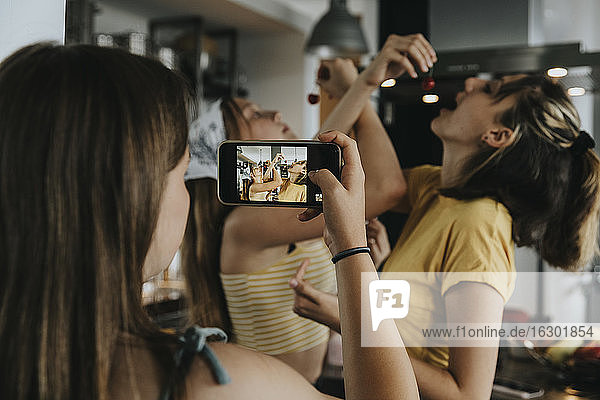 Teenage girl filming friendswith her smartphone  eating cherries