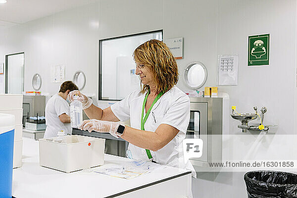 Pharmazeutin hält Flasche in Behälter auf Tisch in Labor