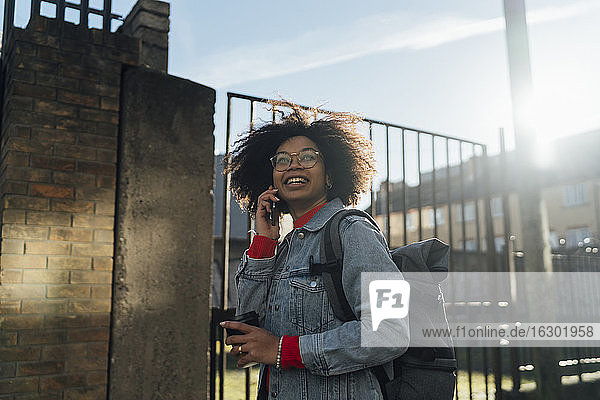 Afro woman talking over mobile phone while standing against sky during sunny day