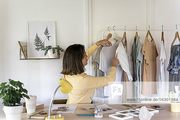 Junge Modedesignerin betrachtet Kleidung  die auf einem Regal im Laden hängt