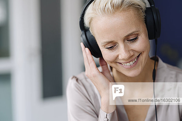 Close-up of smiling businesswoman listening music over headphones looking down in office