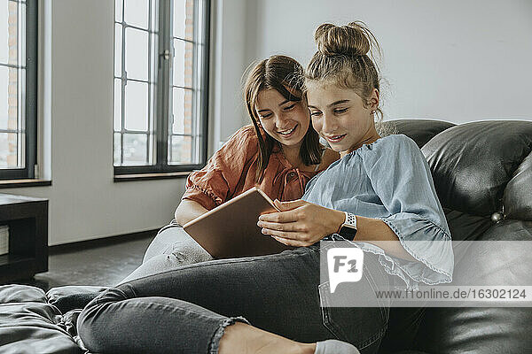 Friends using digital tablet while relaxing on sofa at home