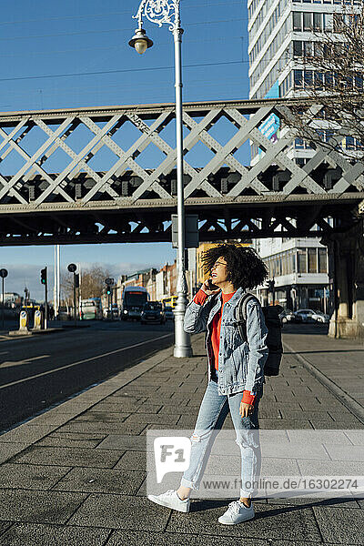 Afro-Frau spricht über Handy  während sie auf dem Bürgersteig in der Stadt steht