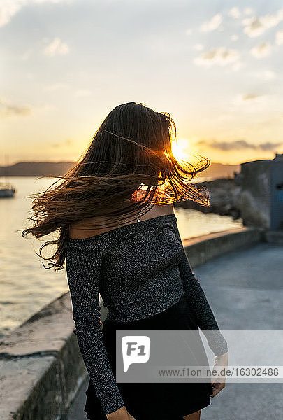 Frau  die sich die Haare zuwirft  während sie bei Sonnenuntergang an der Promenade steht