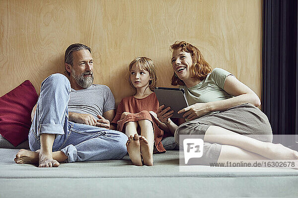 Fröhliche Frau mit digitalem Tablet  die sich mit ihrer Familie auf dem Bett zu Hause entspannt