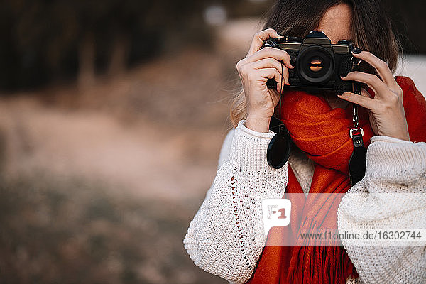 Young woman taking photo from camera while standing in forest