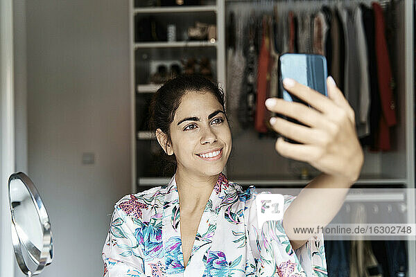 Lächelnde Frau nimmt Selfie auf Smartphone zu Hause
