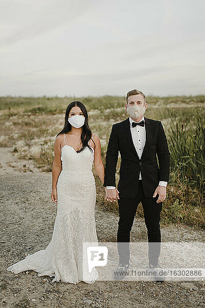 Bride and groom with protective face mask standing in field during COVID-19