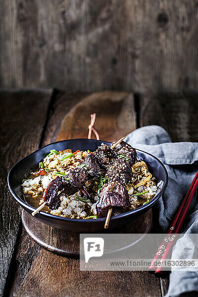 Schüssel mit verzehrfertigem Teriyaki-Reis mit Chinakohl und gegrillten Rindfleischspießchen