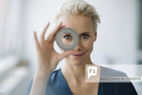 Close-up of smiling businesswoman looking through object in office