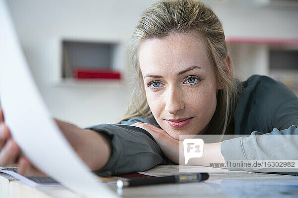 Porträt einer Frau  die sich im Büro an einen Schreibtisch lehnt und Papier hält