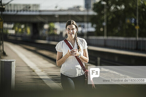 Schöne junge Frau hört Musik über ihr Handy  während sie auf dem Bahnsteig spazieren geht