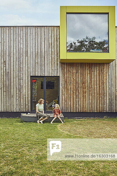 Mutter und Tochter sitzen vor einem kleinen Haus