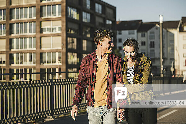 Lächelndes junges Paar hält sich beim Spaziergang in der Stadt an den Händen
