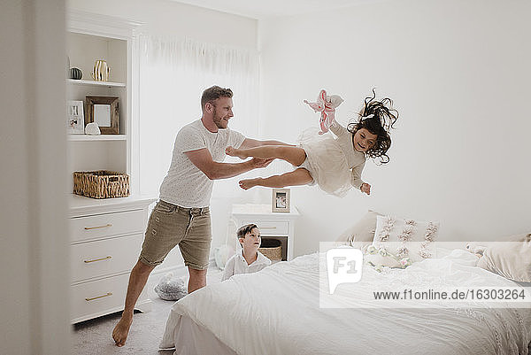 Verspielter Vater wirft Tochter über Bett  während Sohn im Schlafzimmer sitzt