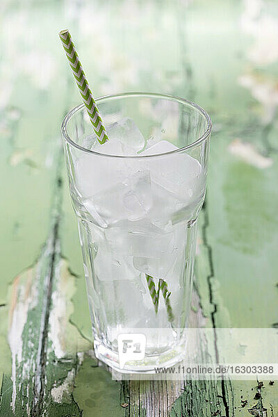 Glas mit Eiswürfeln und Trinkhalm auf Holztisch  Nahaufnahme