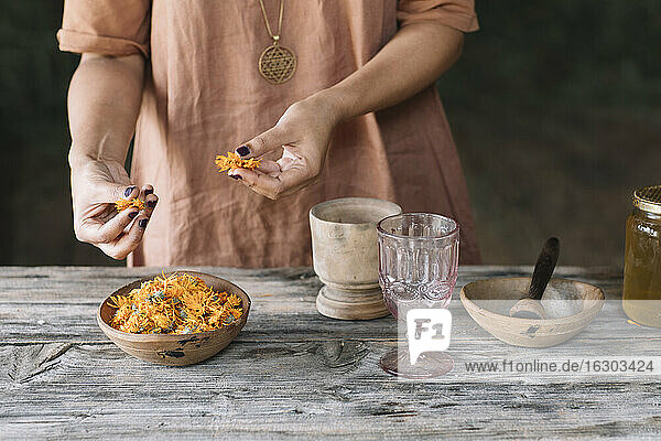 Mittelteil einer erwachsenen Frau  die frische orangefarbene Blumen aus einer Schale auf einem Holztisch auswählt