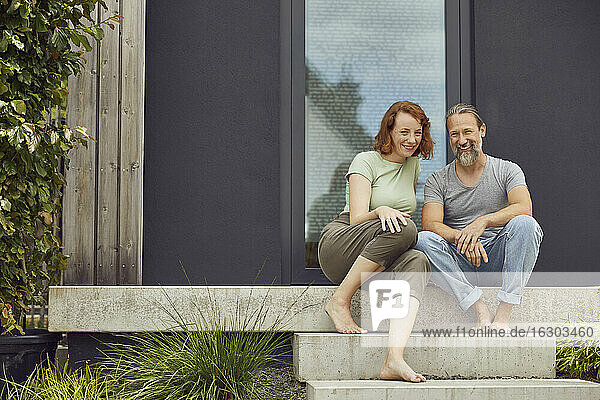 Lächelndes Paar sitzt auf den Stufen vor einem kleinen Haus