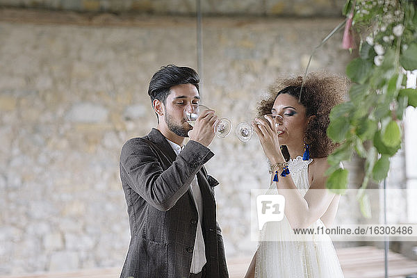 Braut und Bräutigam trinken Wein  während sie im Raum stehen