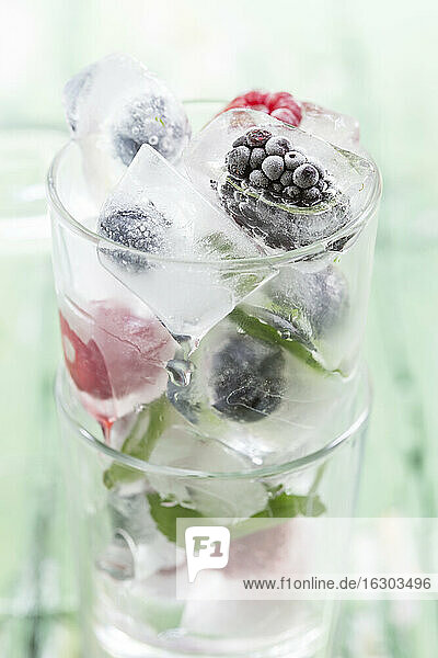 Glas mit Beeren in Eiswürfeln mit Minzblättern auf Holztisch  Nahaufnahme