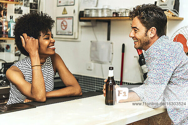 Man holding beer bottle flirting with smiling female bartender at bar counter