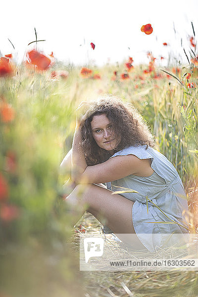 Beautiful woman with hand in hair sitting in poppy field