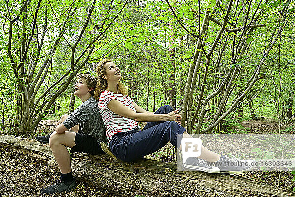 Nachdenkliche Mutter und Sohn sitzen Rücken an Rücken auf einem umgestürzten Baum im Wald