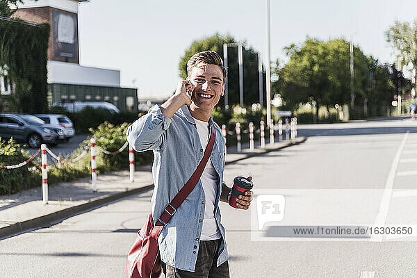 Smiling young man talking on mobile phone while crossing street in city