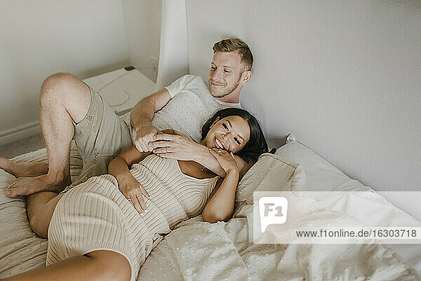 Lächelnde Frau liegt mit männlichem Partner über dem Bett im Schlafzimmer