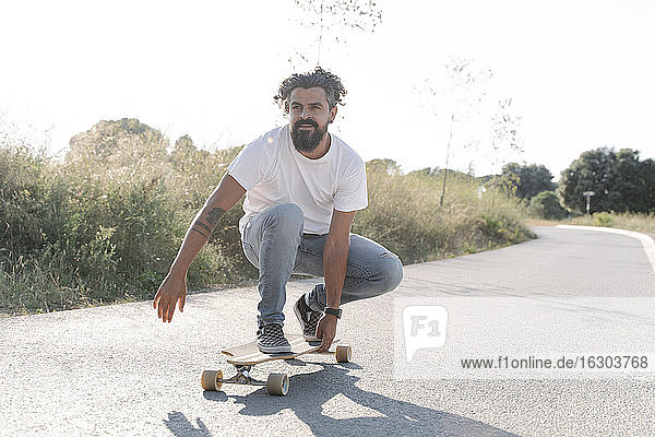Handsome bearded mature man skateboarding on road against clear sky