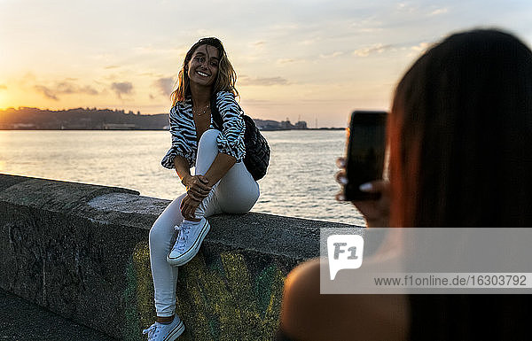 Ein Freund fotografiert eine Frau  die auf einer Stützmauer an der Promenade sitzt